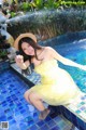 A woman in a yellow dress and straw hat sitting on the edge of a pool.