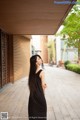 A woman in a black dress standing on a sidewalk.