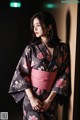 A woman in a black and pink kimono leaning against a wall.