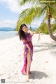 A woman standing on a beach next to a palm tree.