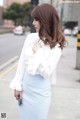 A woman in a white shirt and blue skirt is walking down the street.