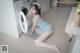 A woman in a blue dress sitting on the floor next to a washing machine.