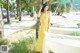 A woman in a yellow dress leaning against a tree.