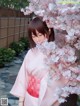 A woman in a pink kimono standing next to a tree.