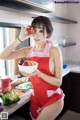 A woman in a red apron holding a bowl of fruit.