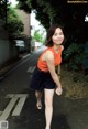 A woman in an orange top and black shorts walking down a street.