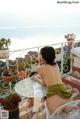 A naked woman sitting at a table on a balcony.