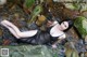 A woman in a black dress laying on a rock in a stream.