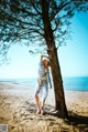 A woman standing next to a tree on a beach.