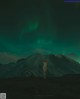 A nude woman standing in front of a green aurora borealis.