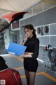 A woman standing next to a red car holding a blue folder.