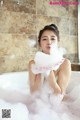 A woman sitting in a bathtub with foam on her face.