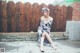 A woman sitting on the ground in front of a wooden fence.