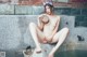 A naked woman sitting on a stone ledge holding a bowl.