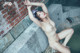 A naked asian woman leaning against a brick wall.