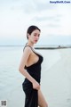 A woman in a black dress standing on a beach.