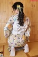 A woman in a kimono sitting on a mat in a room.