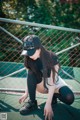 A woman crouching down on a tennis court wearing a baseball cap.