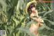 A naked woman in a straw hat standing in a field of corn.