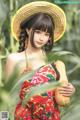 A woman in a red dress and straw hat holding a squash.