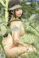 A naked asian woman sitting in a field of tall grass.