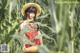 A woman in a red dress and straw hat standing in a corn field.