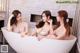 A group of three women sitting in a bathtub in a bathroom.