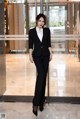 A woman in a black suit standing in front of a glass door.