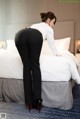 A woman in a white shirt and black pants standing on a bed.