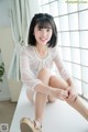 A woman sitting on top of a white table next to a window.