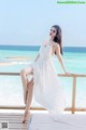 A woman in a white dress sitting on a balcony overlooking the ocean.