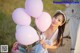 A young woman holding a bunch of pink and purple balloons.