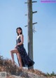 A woman leaning against a telephone pole on a beach.