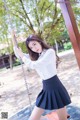 A woman in a white shirt and black skirt on a swing.