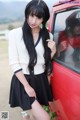 A woman leaning against a red car with her reflection in the window.