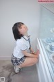 A woman in a school uniform crouching down in front of a display case.