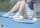 A woman sitting on a tennis court next to a tennis racket.