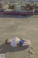 A woman laying on top of a building with a city in the background.