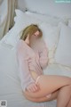 A woman sitting on a bed in a pink sweater.