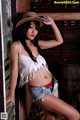 A woman in a cowboy hat leaning against a barn door.