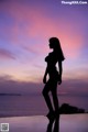 A woman standing on the edge of a swimming pool at sunset.