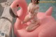 A woman in a white bathing suit sitting on an inflatable flamingo.