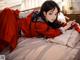 A woman in a red kimono laying on a bed.