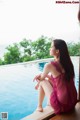 A woman in a pink dress sitting by a swimming pool.