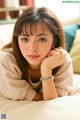 A woman laying on top of a bed with her hand on her chin.