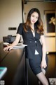 A woman in a business suit leaning on a desk.