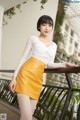 A woman in a white top and yellow skirt posing for a picture.