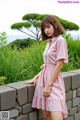 a woman in a pink dress leaning against a stone wall