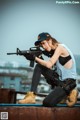 A woman sitting on top of a building holding a rifle.