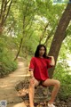 A woman in a red shirt is sitting on a stone bench.